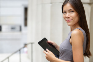 Businesswoman lawyer using tablet pc computer outside in front of courthouse smiling happy looking at camera. Beautiful young mixed race Caucasian / Asian Chinese professional woman.