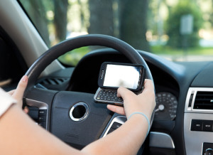 Closeup of a smart phone with a female hand texting and driving.